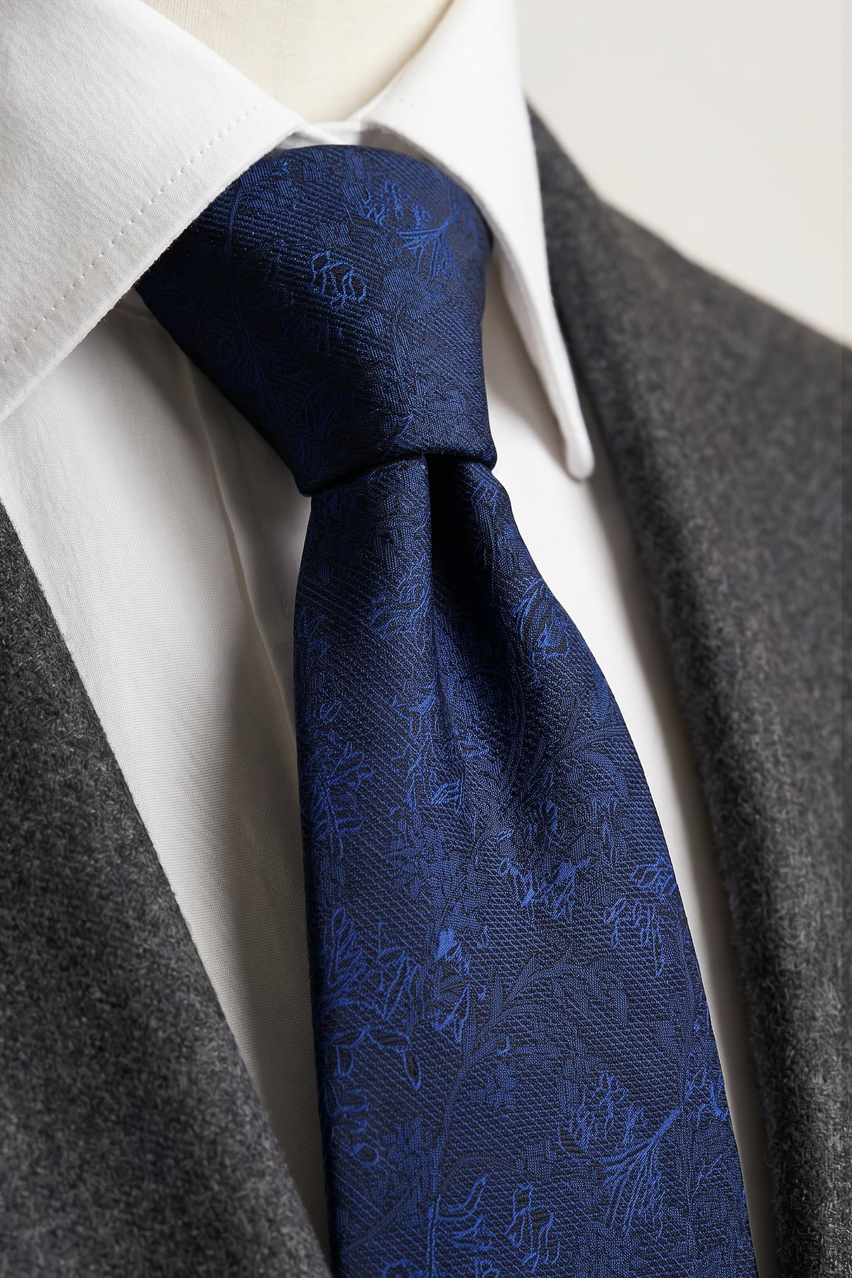 Beyaz gömlek ve gri ceket üzerinde bağlanmış kendinden desenli lacivert erkek kravat düğümü